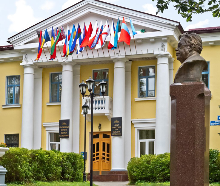 Сграда с международни флагове и бюст на пиедестал отпред.