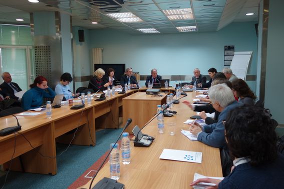 Група лица в официално облекло, присъстващи на конференция в зала с кръгла маса.