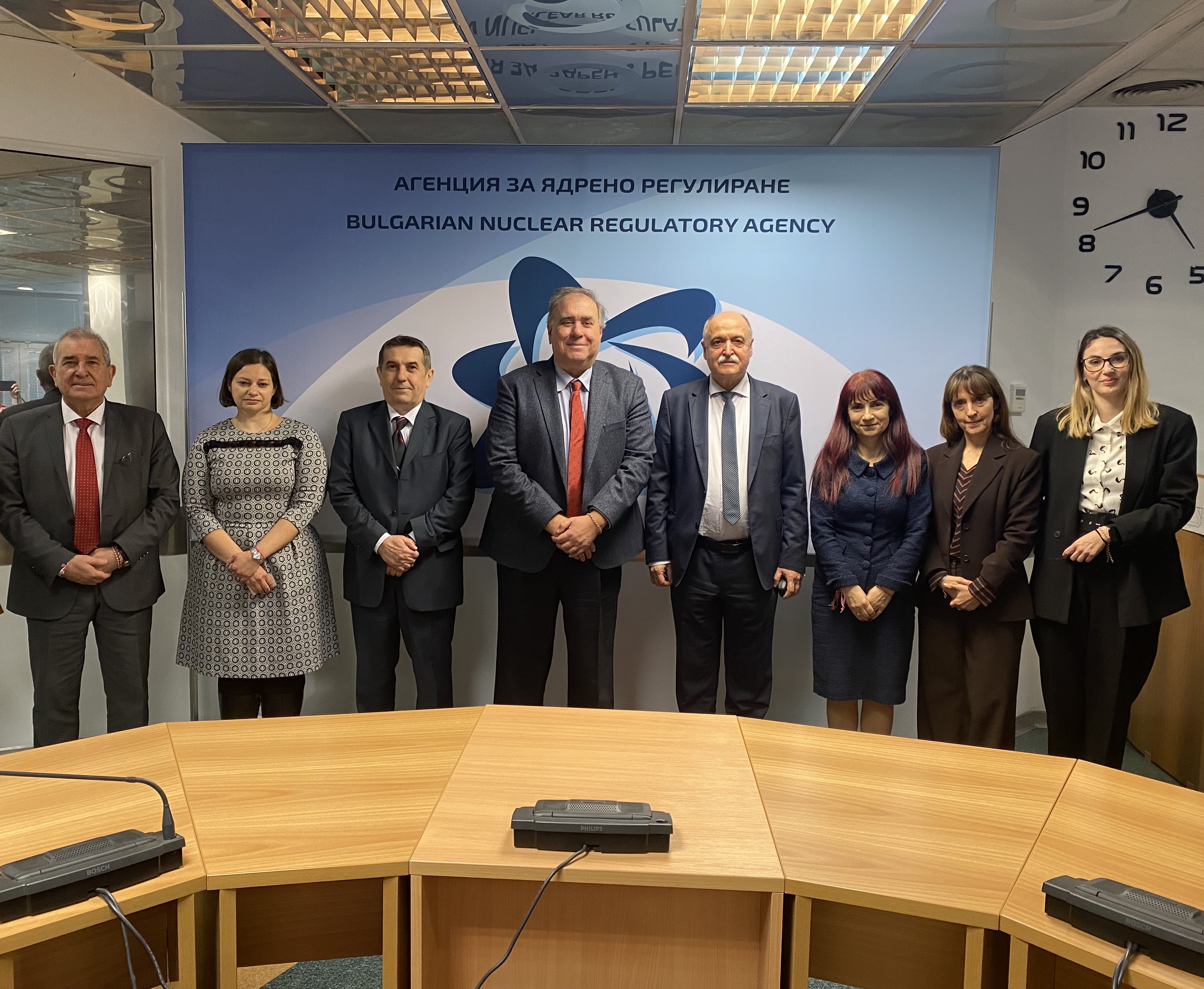 Група от осем лица в официално облекло пред табела на Българската агенция за ядрено регулиране.