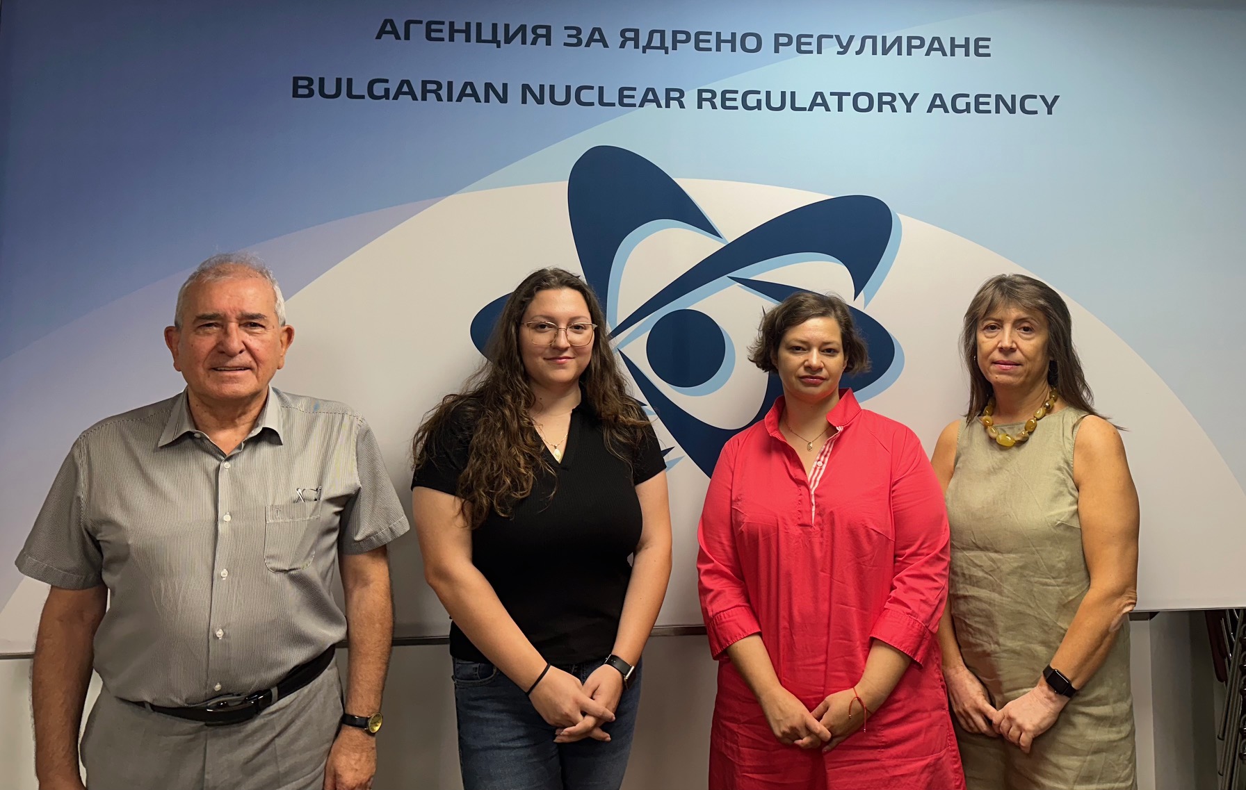 Четири лица пред таблицата на Агенцията за ядрено регулиране на България, усмихнати, с лого зад тях.