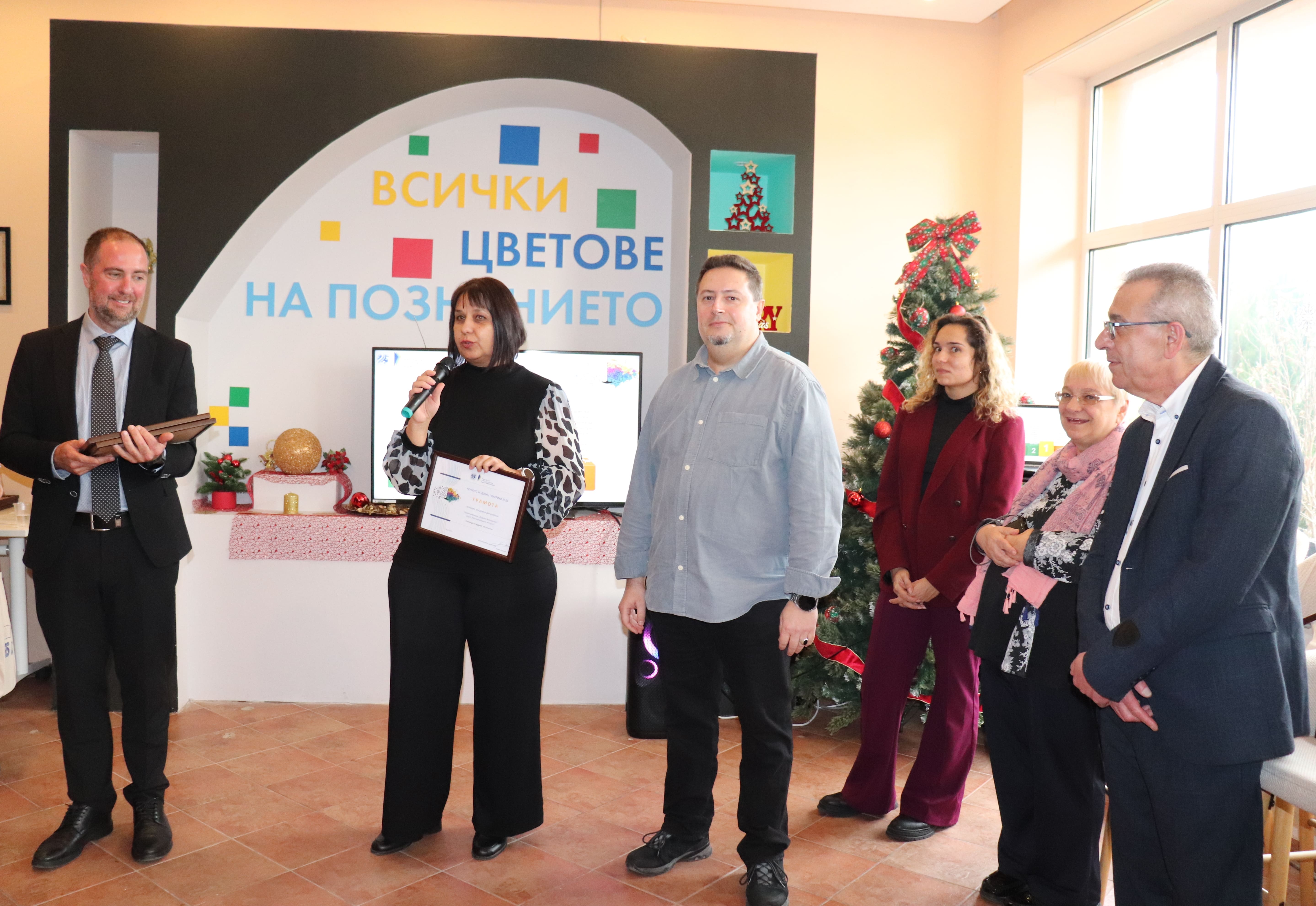 Шестима души край коледна елха; служител на АЯР представя награда от конкурса за добри практики, присъстват колеги.