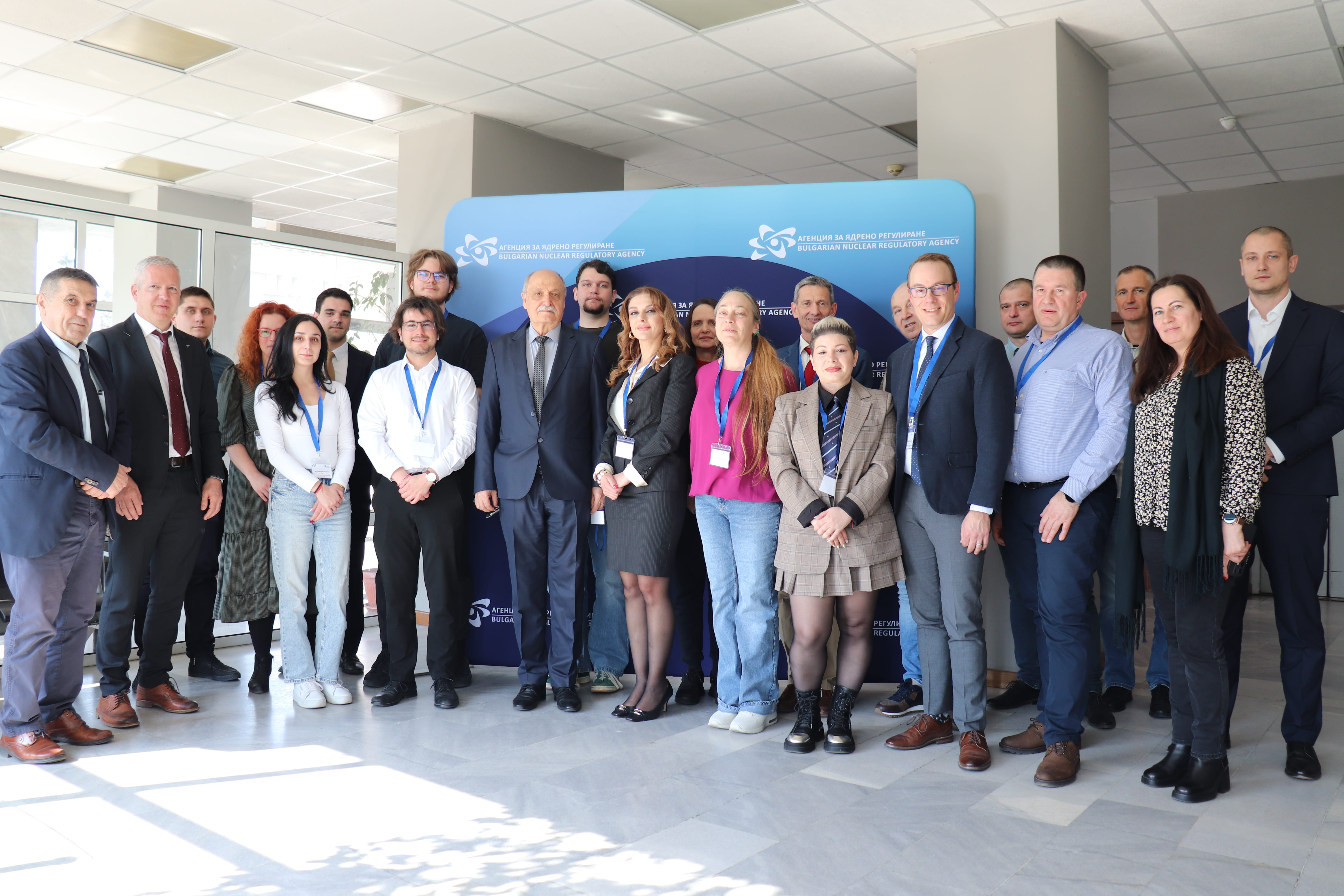 Група професионалисти в офис лоби пред син фон след обучителен семинар по ядрена сигурност.