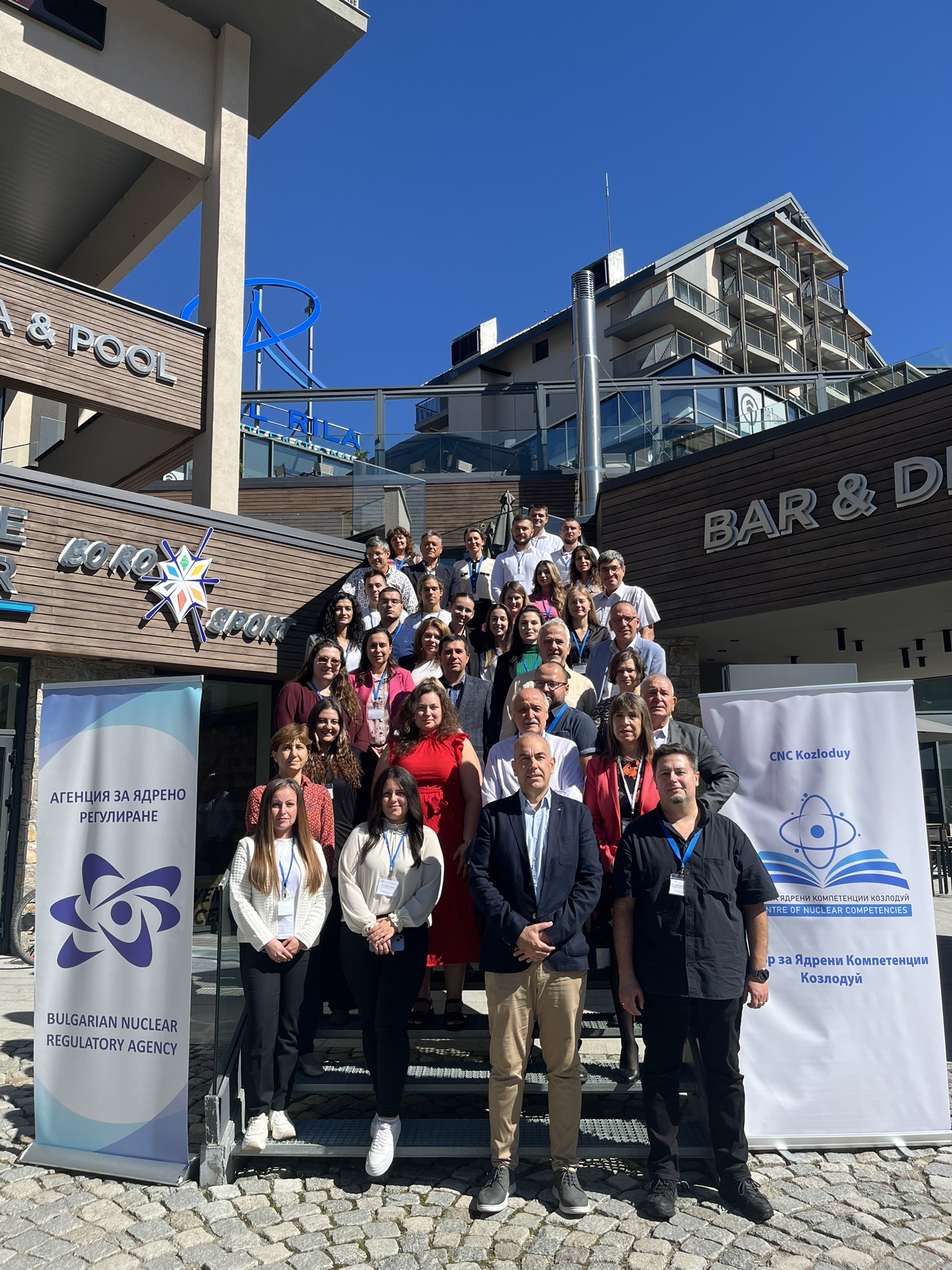 Групова снимка на участниците в училище по ядрено регулиране пред хотел, с две банери от двете страни.