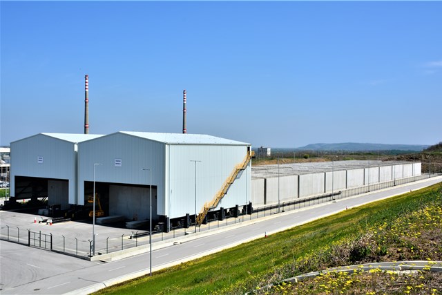 Две големи индустриални складови сгради с комини и ограден двор, разположени до път при ясно време.