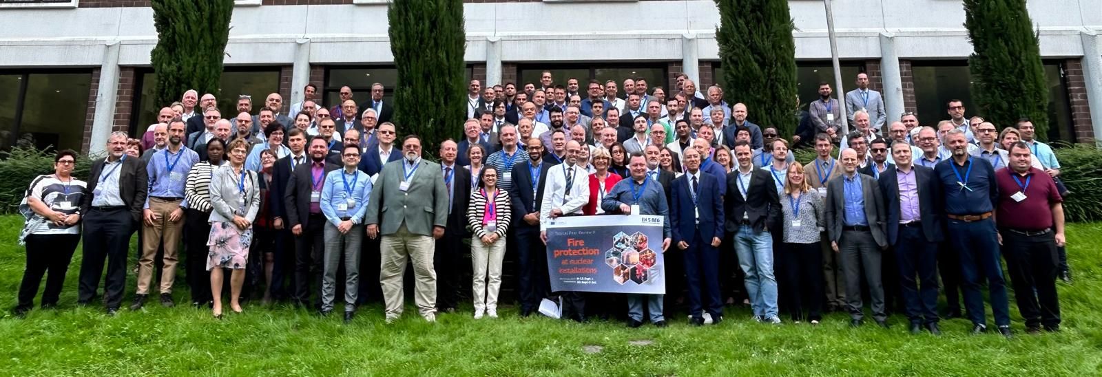 Голяма група хора, разположена на тревна площ пред сградата, позиция за групова снимка.
