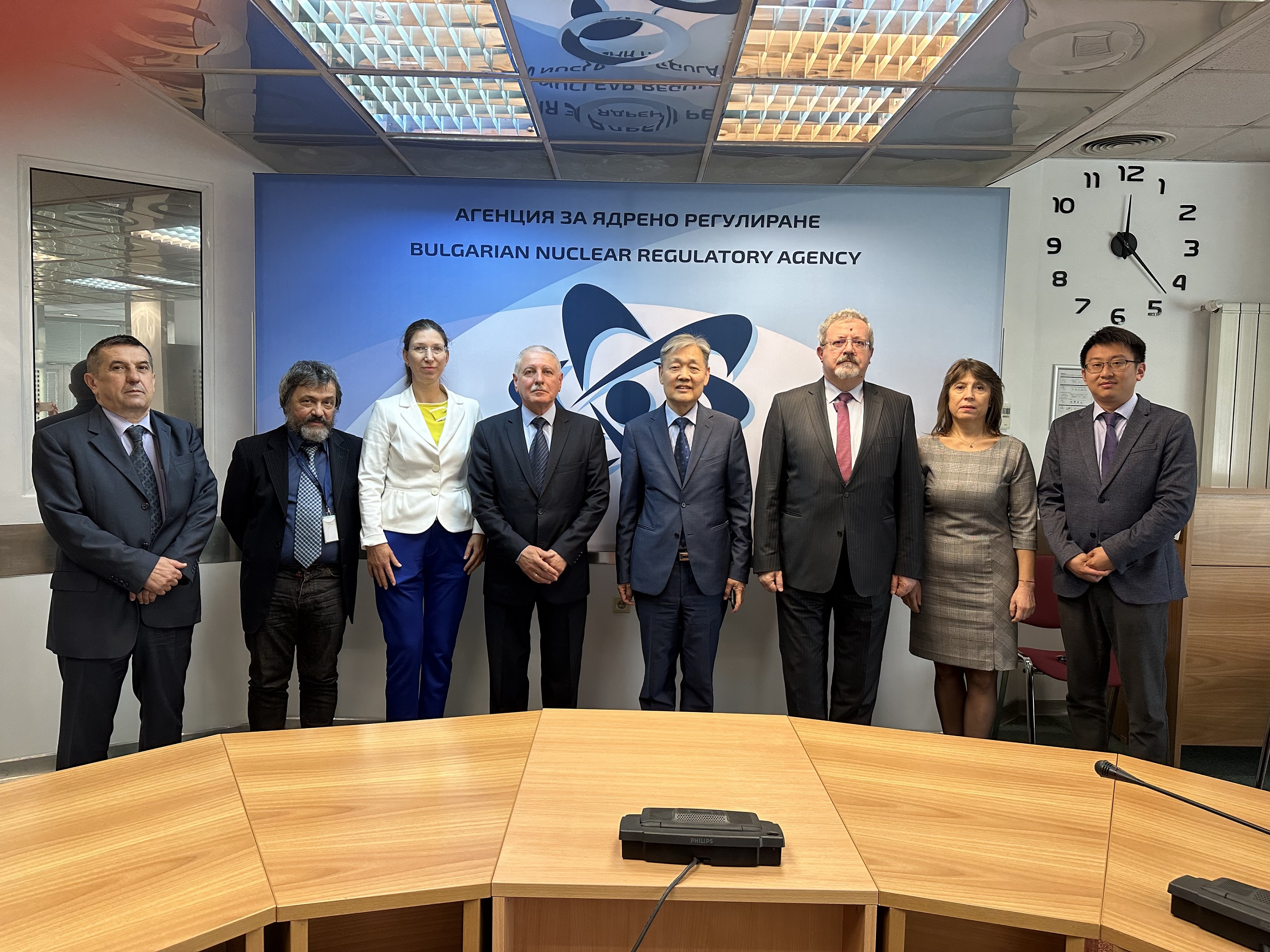 Група от осем лица в официално облекло позират в офис пред надпис "Агенция за ядрено регулиране на Република България".